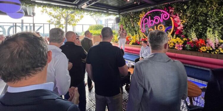 Photo of a woman holding a microphone while standing on a platform at an operational technology cyber security meetup in a bar setting